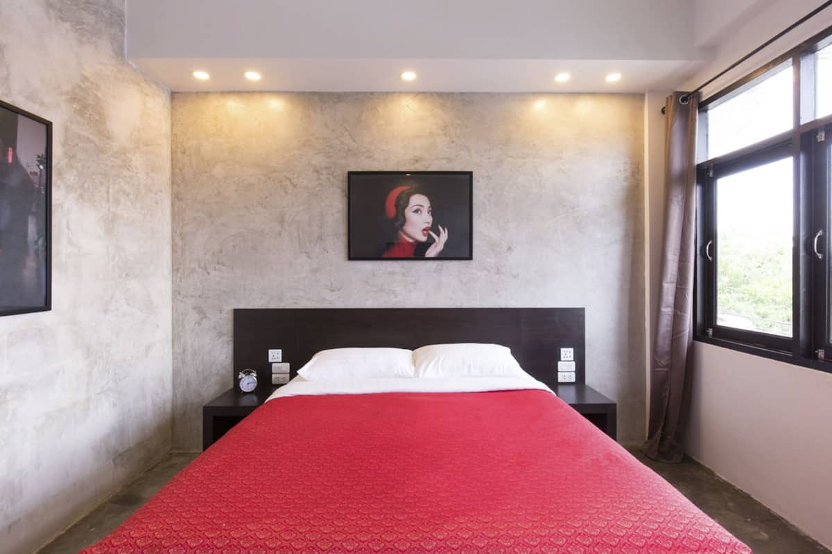 Une chambre à coucher avec un lit, une table de chevet, un tableau encadré au mur et une fenêtre avec des rideaux.