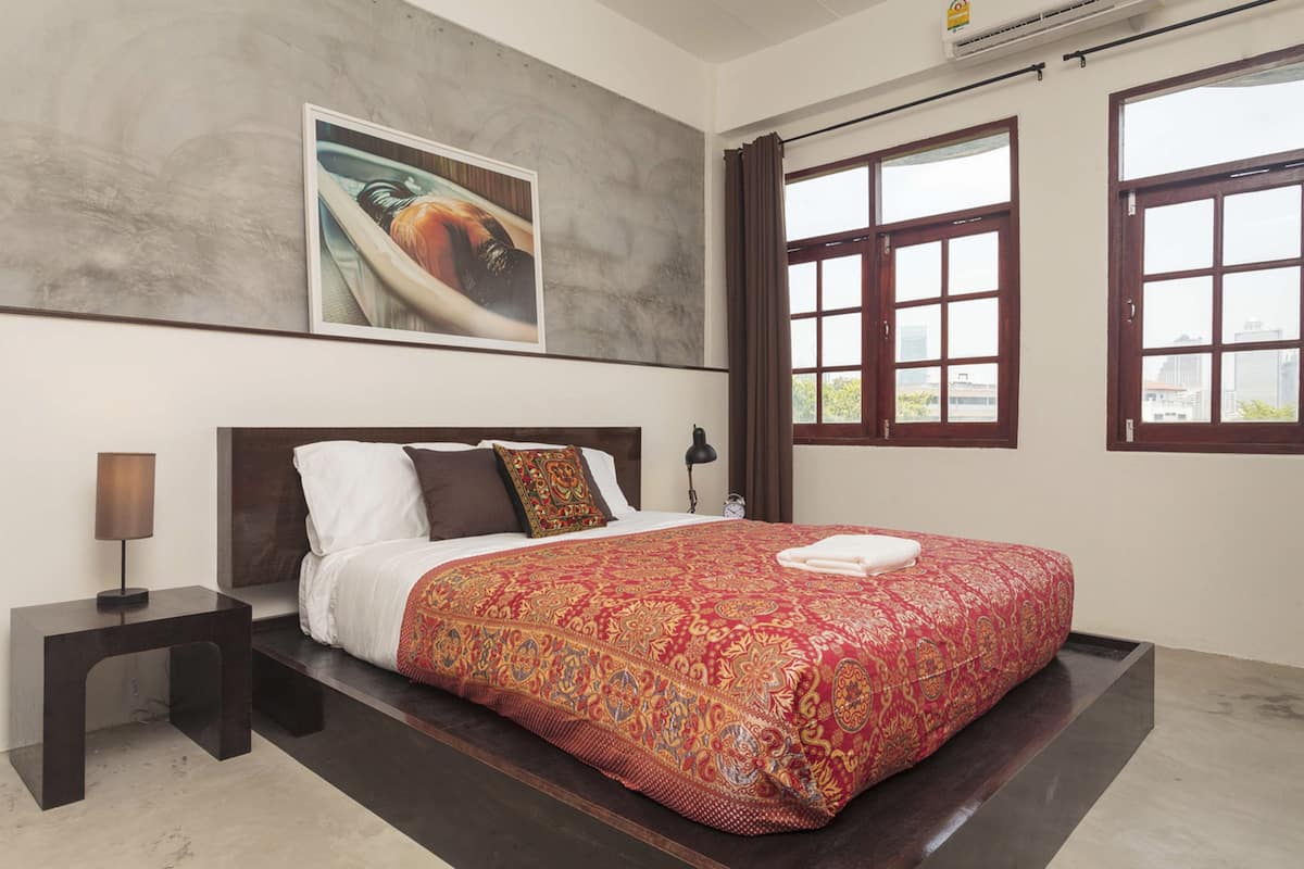 Une chambre d’hôtel avec un grand lit, une table de chevet, un tableau accroché au mur et une fenêtre avec des rideaux.
