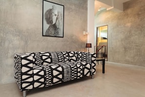 A modern living room with a patterned sofa, a framed artwork on the wall, and a staircase in the background.