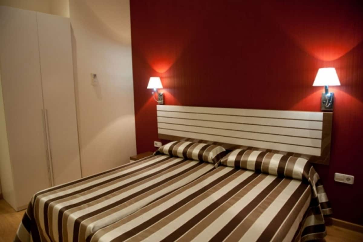 Una cama con ropa de cama a rayas, un cabecero blanco y dos lámparas fijadas a la pared.