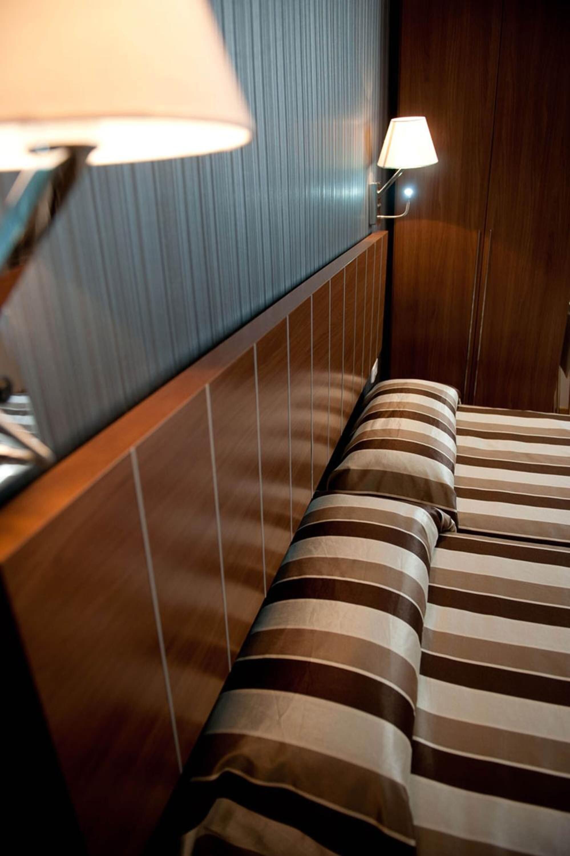 Une chambre d’hôtel avec une tête de lit en bois, une couvre-lit à rayures et deux lampes de chevet.