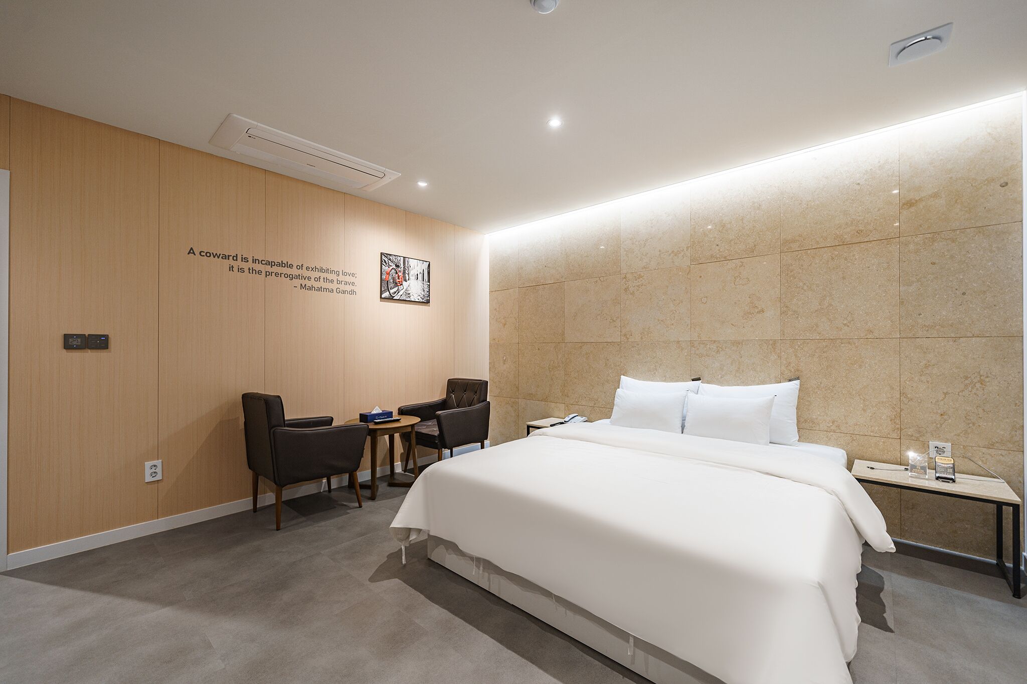 Een moderne hotelkamer met een groot bed, een bureau, twee stoelen, een bijzettafeltje en een wandairconditioner.