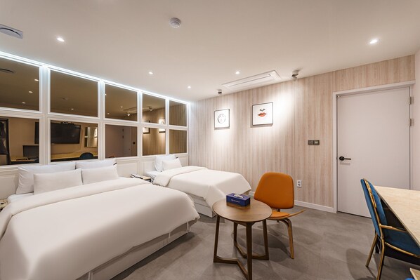 Une chambre d’hôtel avec deux lits, une petite table et une chaise, et une porte.