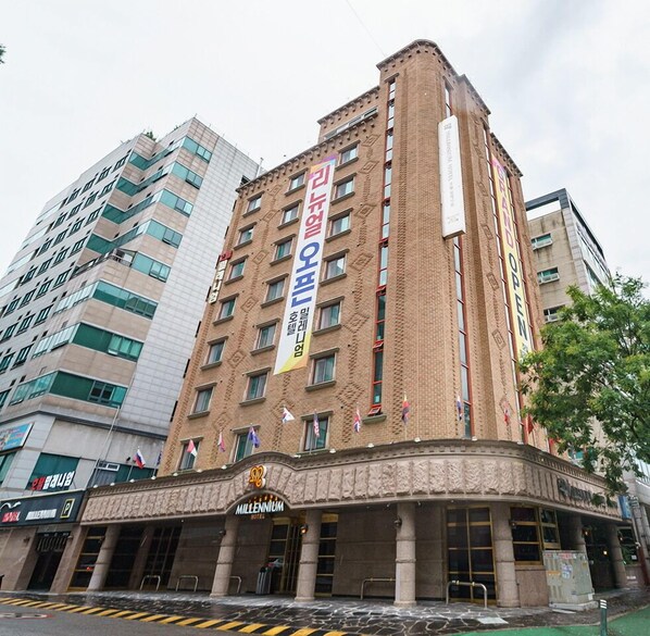 A brick building with multiple floors, a prominent sign for 'Millennium Hotel', and several flags. - Hotel Millennium (Goyang)