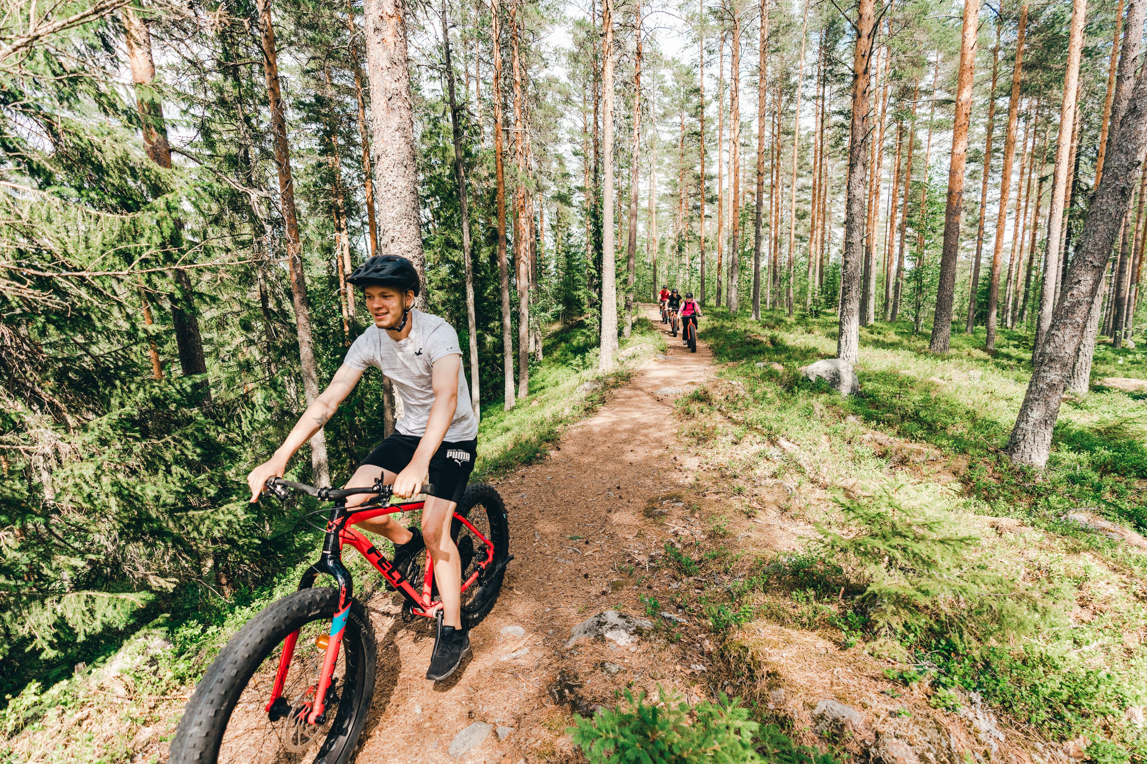 A forest trail with a mountain bike rider and another cyclist in the distance.