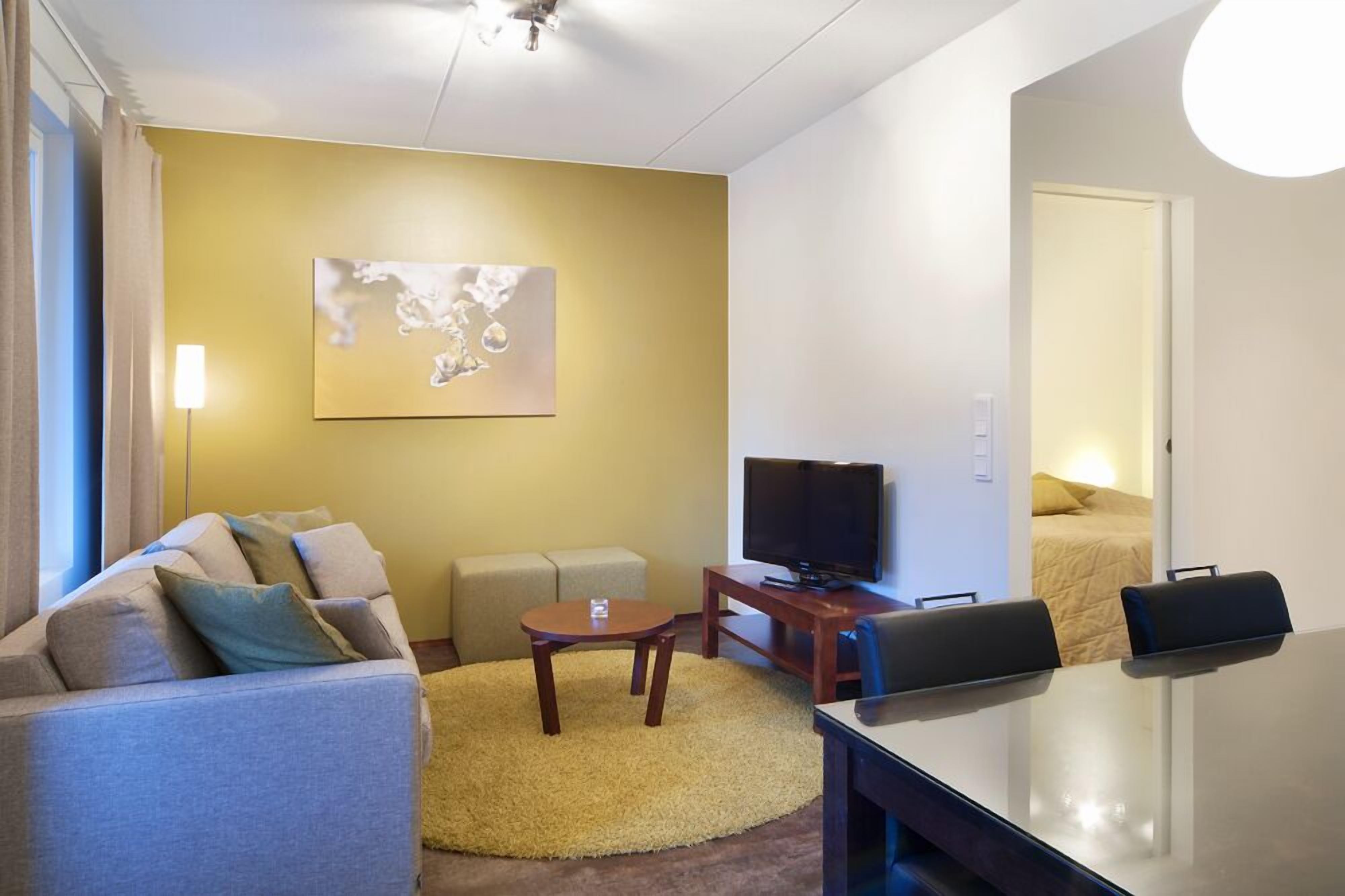 Una habitación de hotel moderna con un sofá, una mesita redonda, un televisor y una cama.