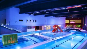 Una piscina interior con tobogán, escaleras y puesto de socorrista.