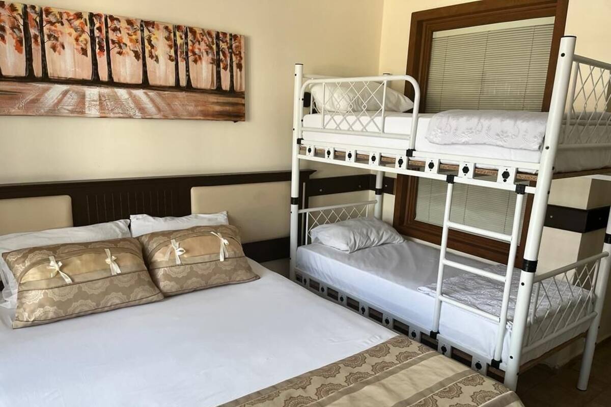 Une chambre avec un lit superposé, un grand tableau au mur, une fenêtre avec des stores et une couvre-lit à motifs.