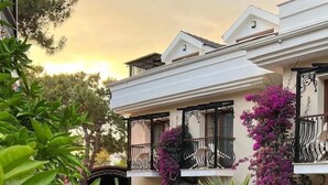 A multi-story building with balconies, surrounded by lush greenery and a brick pathway. - Telmessos Neva Hotel - Halal-Non Alcoholic  Hotel (Fethiye)