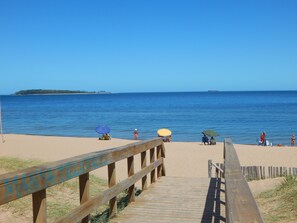 A wooden boardwalk leading to a sandy beach with umbrellas and people. - Apart Hotel Punta Sol (Punta del Este)