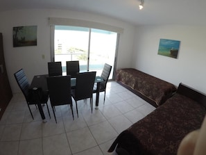 Ein Schlafzimmer mit einem Bett, einem Sofa, einem Esstisch mit Stühlen und einem großen Fenster.