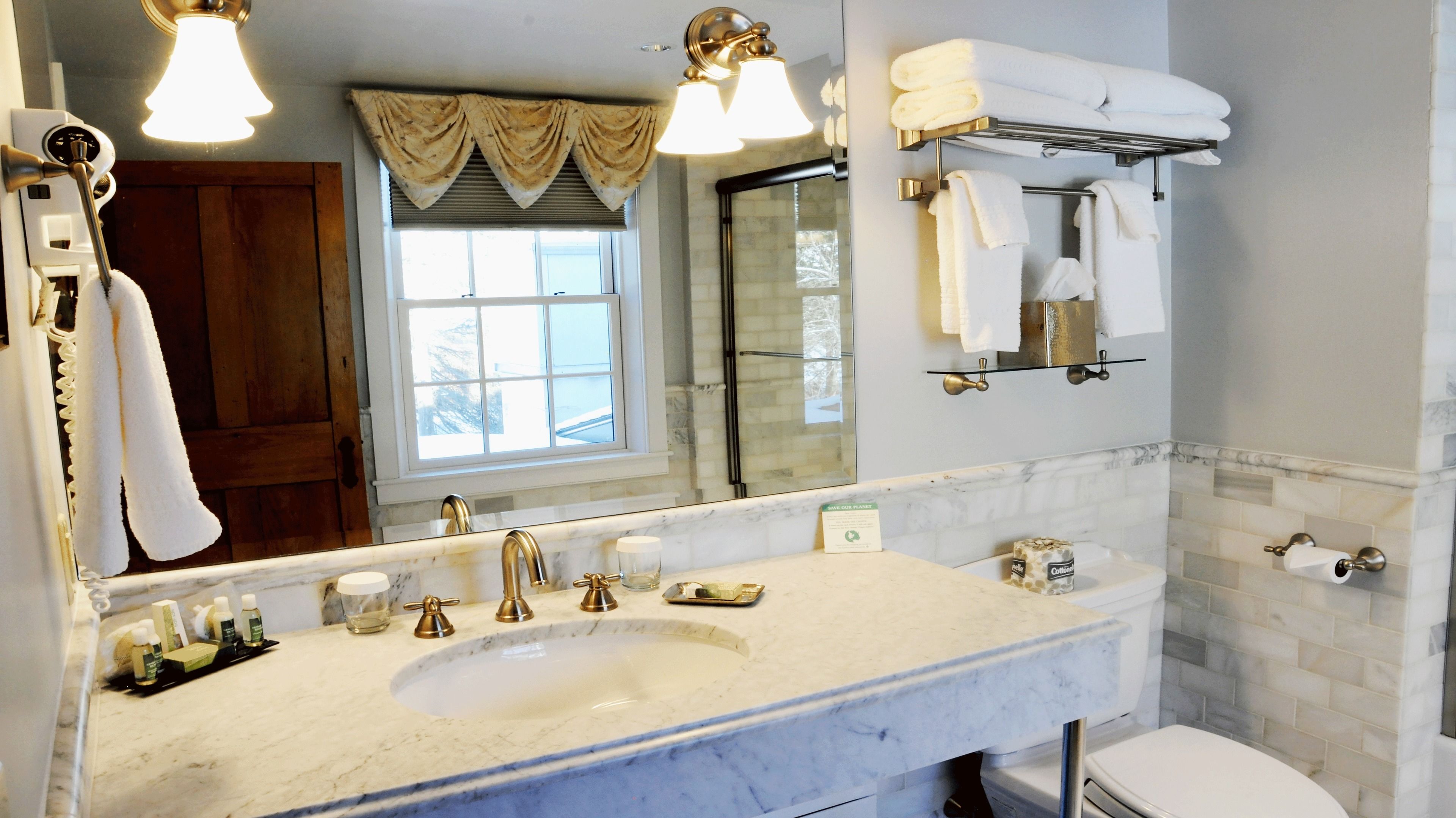 A bathroom with a large mirror, a sink with gold fixtures, a towel rack, and a toilet.