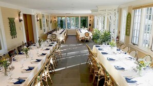 A large banquet hall with long tables set for dining, surrounded by large windows and potted plants. - The Lyme Inn (Lyme)