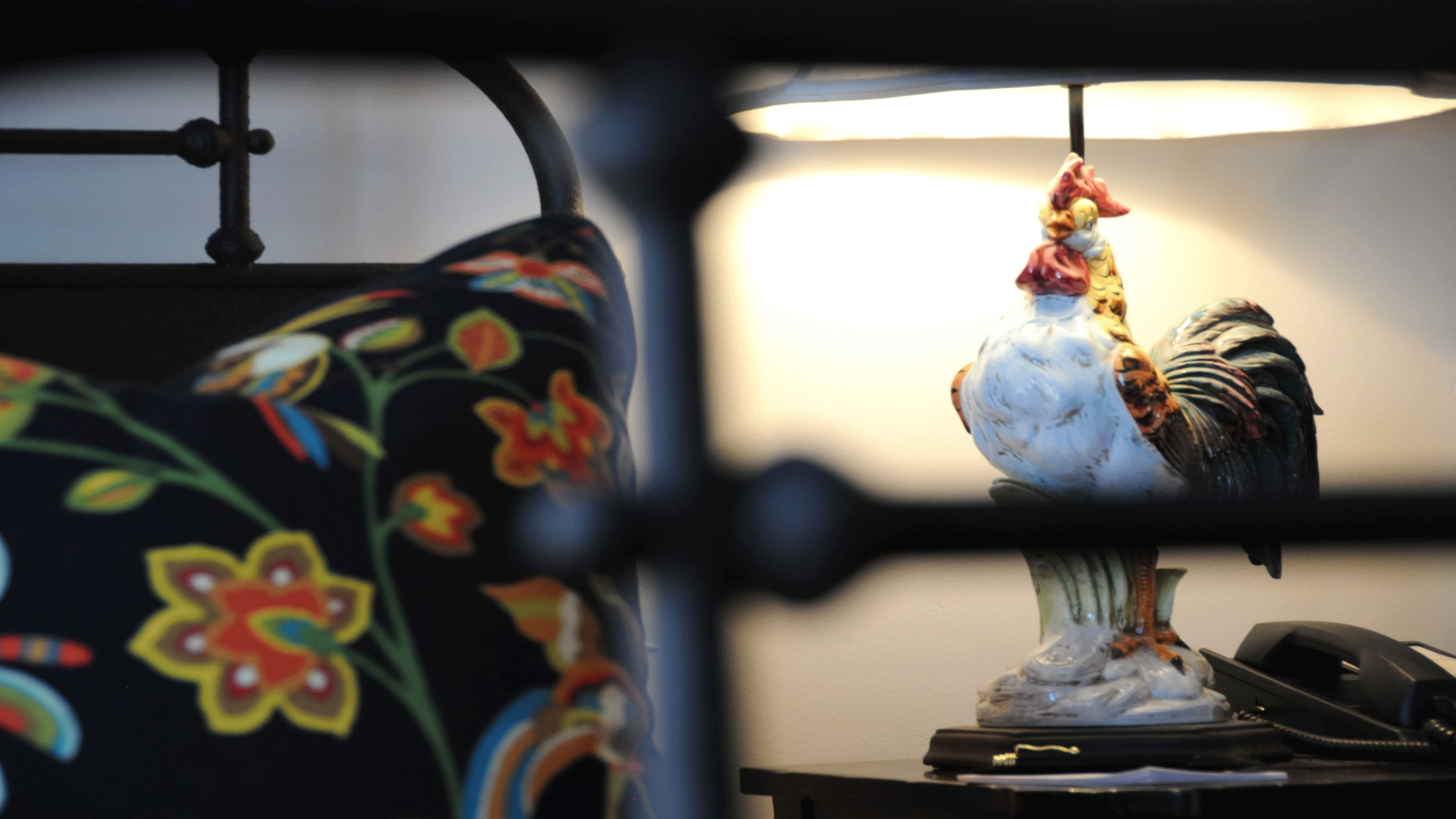 A rooster figurine on a table with a floral-patterned pillow in the foreground.