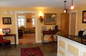 A cozy living room with a fireplace, a coffee table, and a television. There is a dining area with a table and chairs. The room has a warm color scheme and a large window.