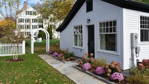 A white single-story house with a black roof, a front porch, and a small garden with pink flowers. - The Lyme Inn (Lyme)
