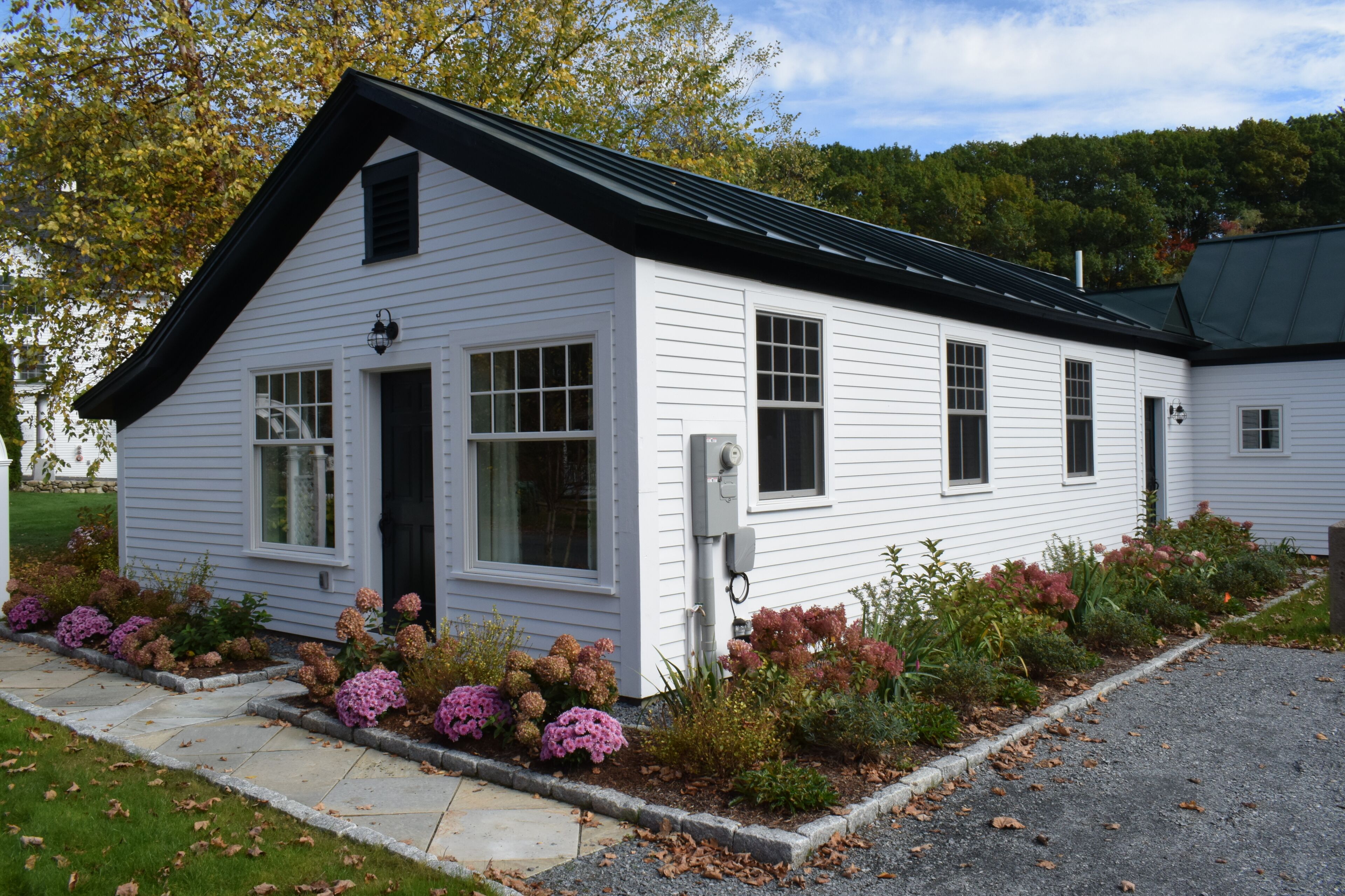 A white single-story house with a black roof, a front door, and a small porch area.