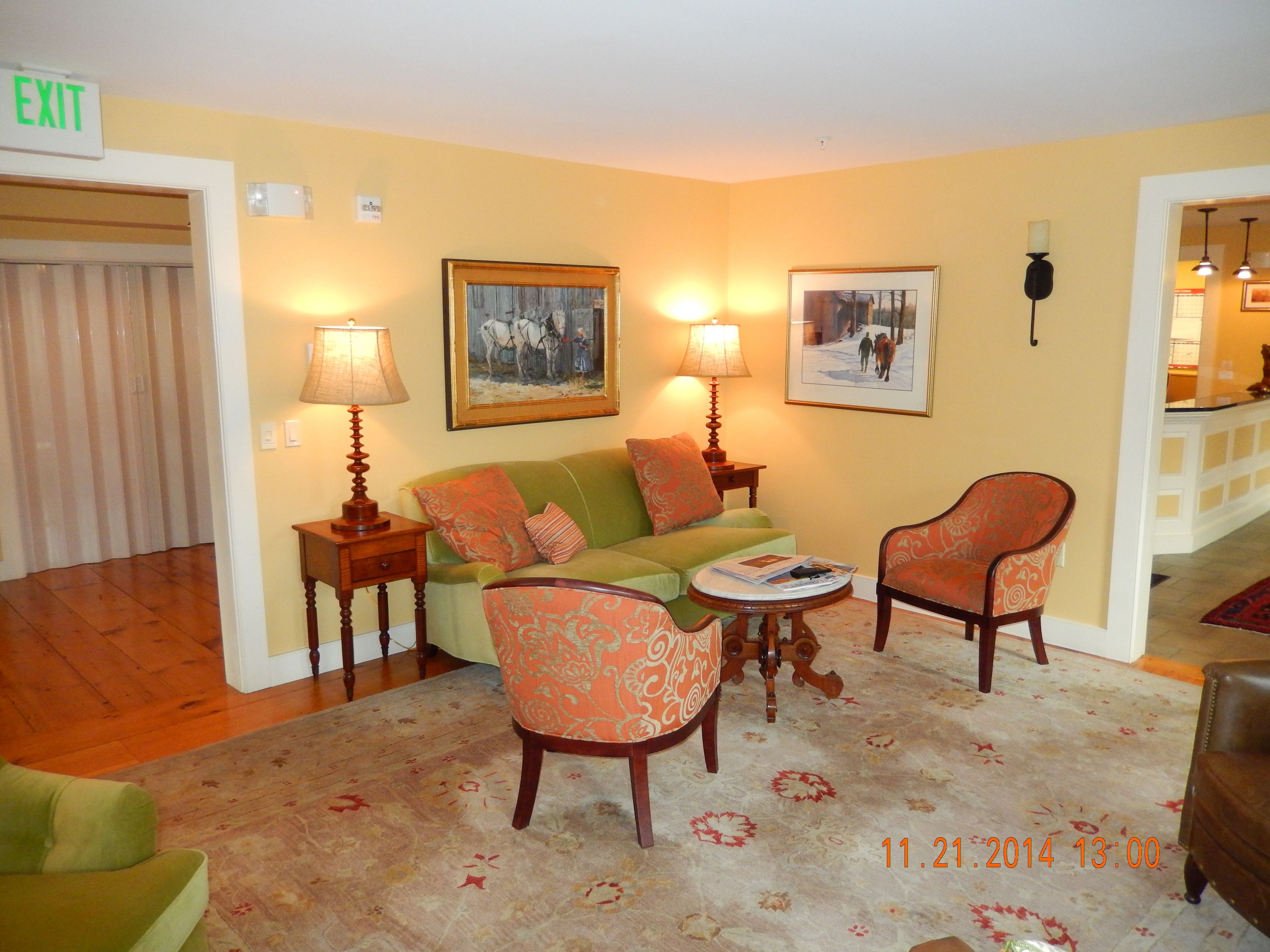A cozy living room with a green sofa, two patterned armchairs, a coffee table, and two lamps.