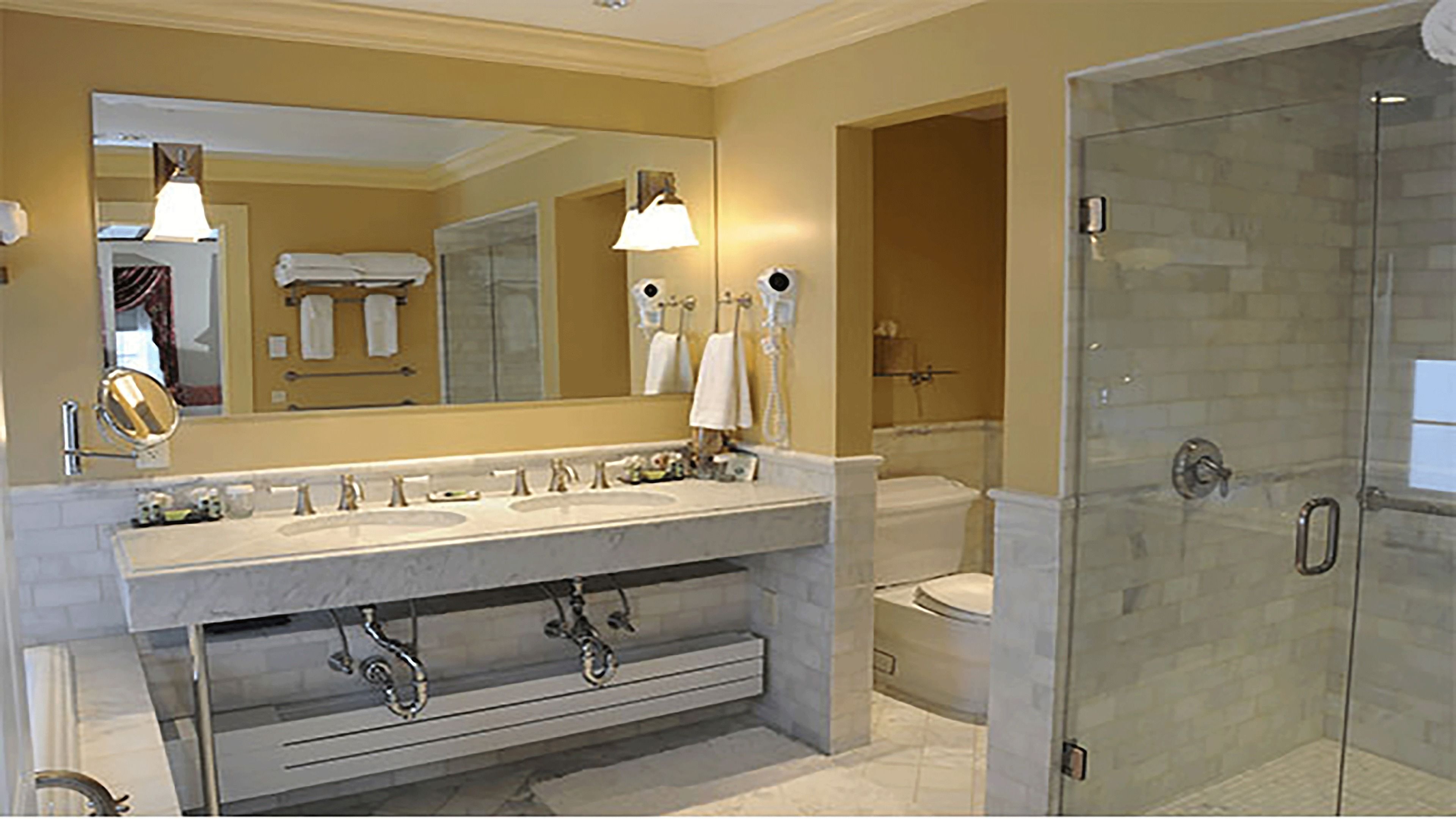 A modern bathroom with a large mirror, dual sinks, a shower, and a glass-enclosed shower area.