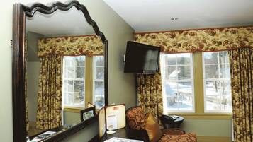 A room with a large mirror, a television mounted on the wall, and two windows with floral curtains.