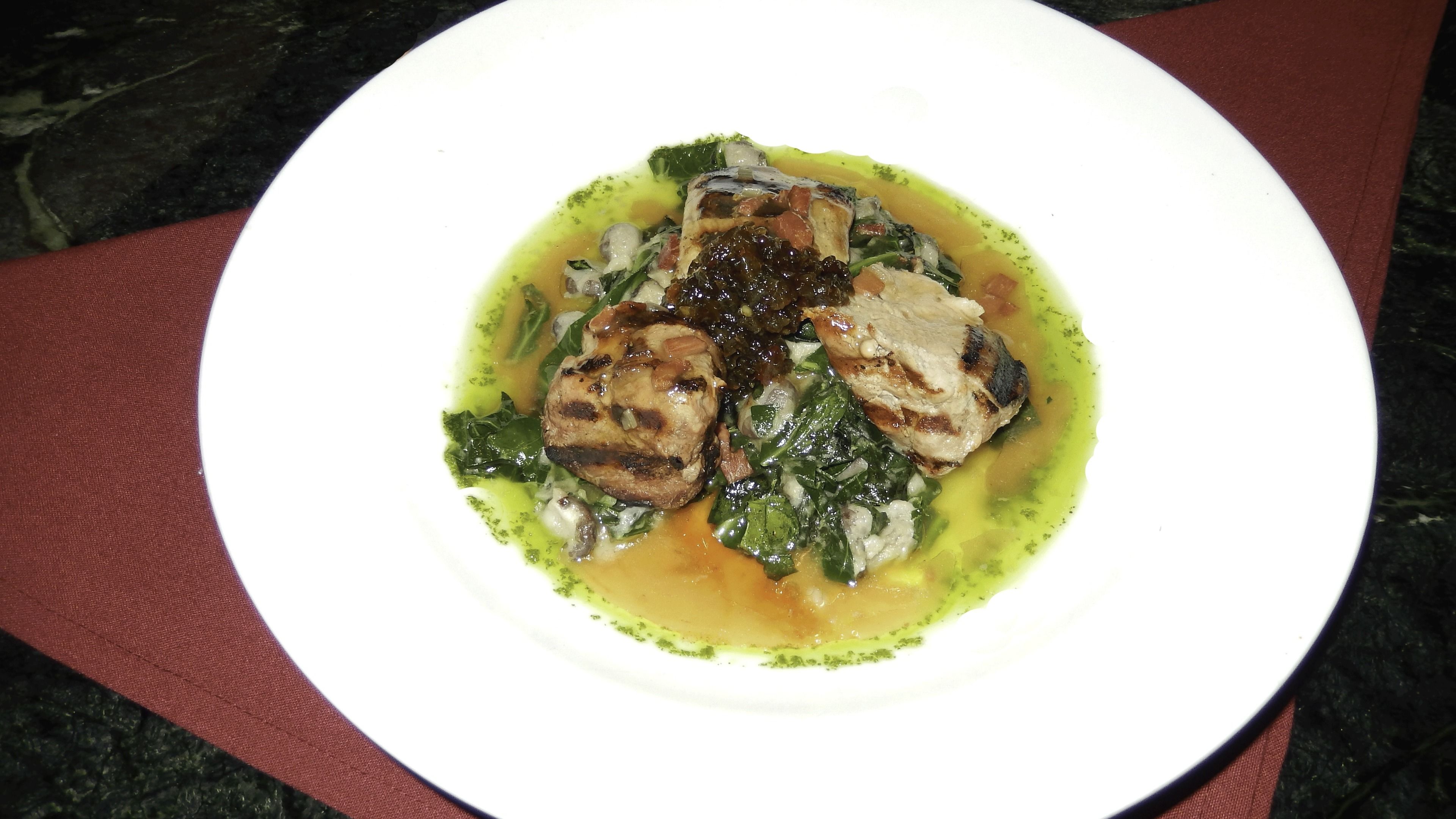 A white plate with a dish of grilled meat and greens on a dark marble surface.