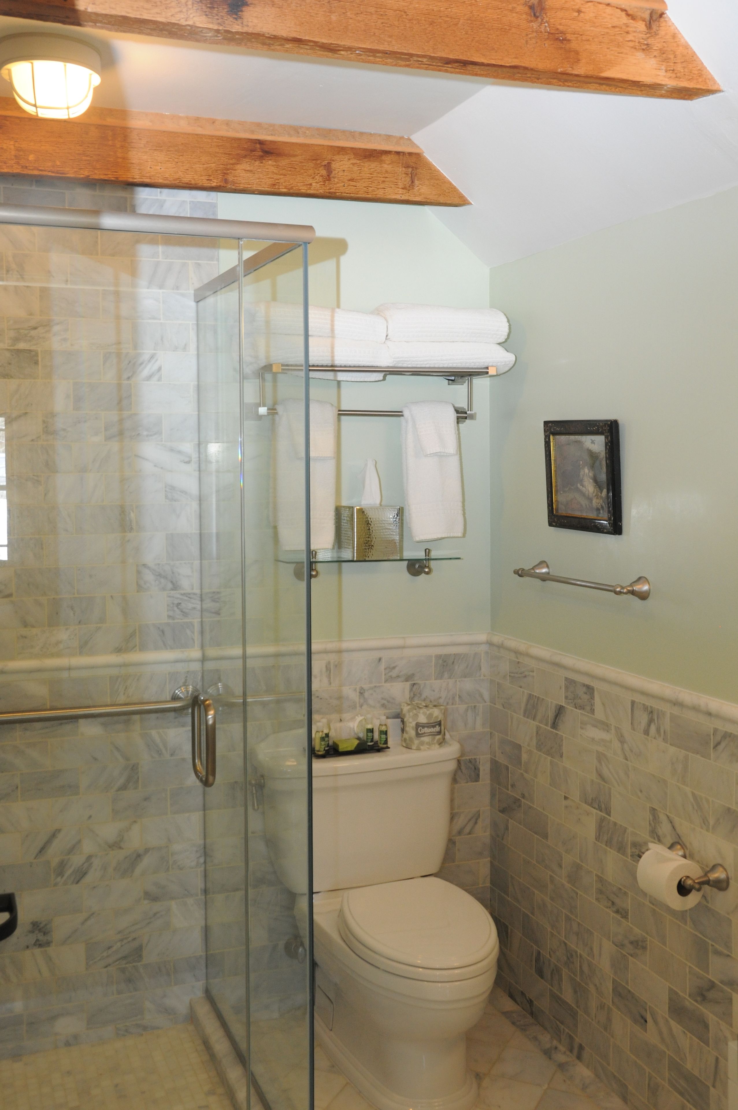 A bathroom with a glass shower enclosure, a toilet, a towel rack, and a framed picture on the wall.