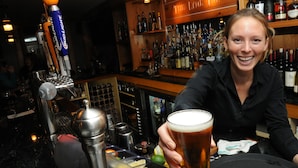 A bar with a beer tap, a variety of bottles, and a person holding a glass of beer. - The Lyme Inn (Lyme)