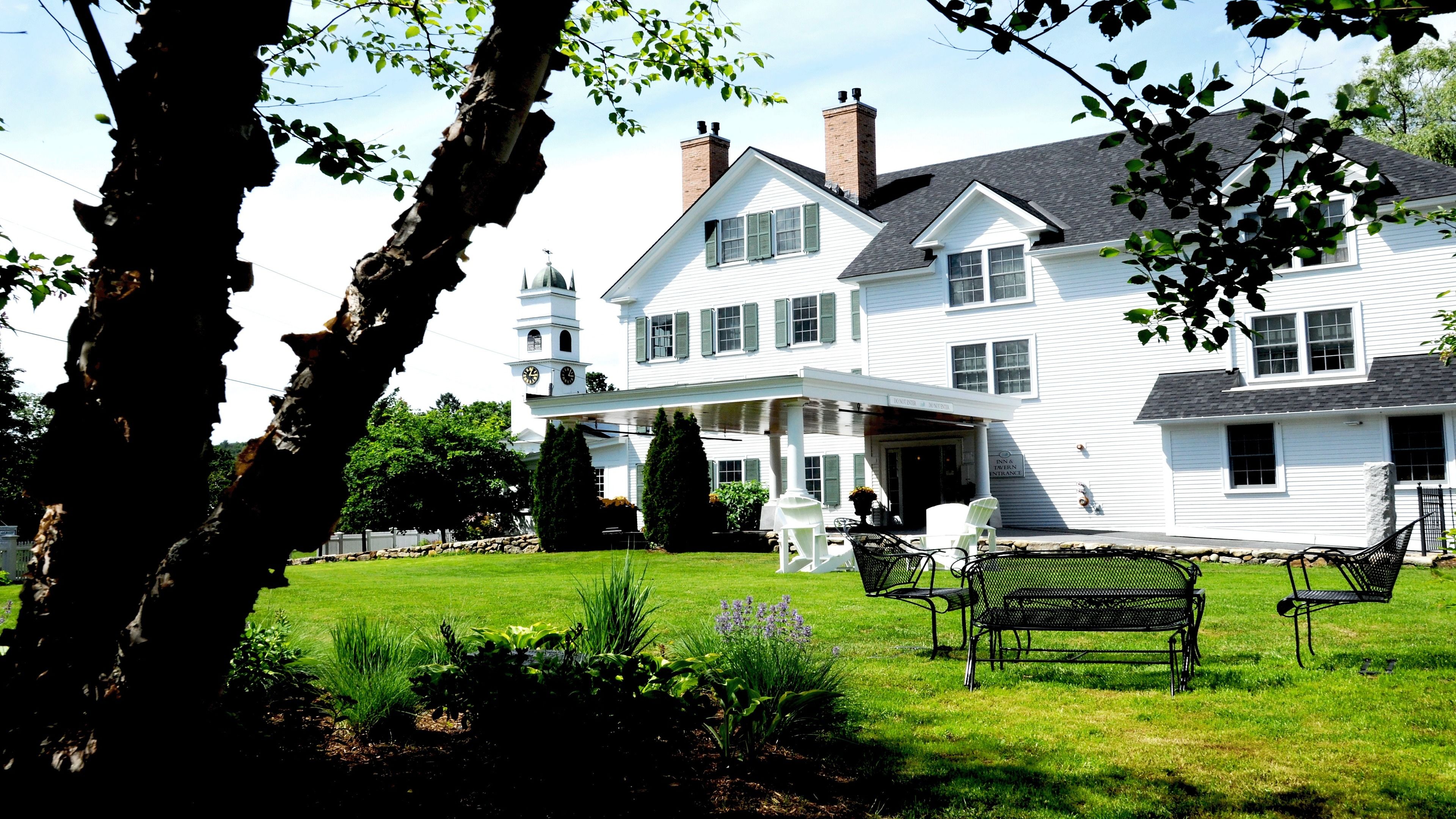 A large white building with a prominent tower, a covered porch, and a well-maintained lawn with benches.