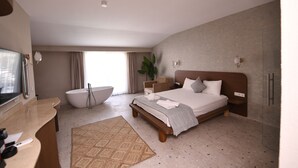 Ein modernes Hotelzimmer mit einem großen Bett, einer Badewanne, einem Schminktisch mit Spiegel und einem großen Fenster mit Vorhängen.