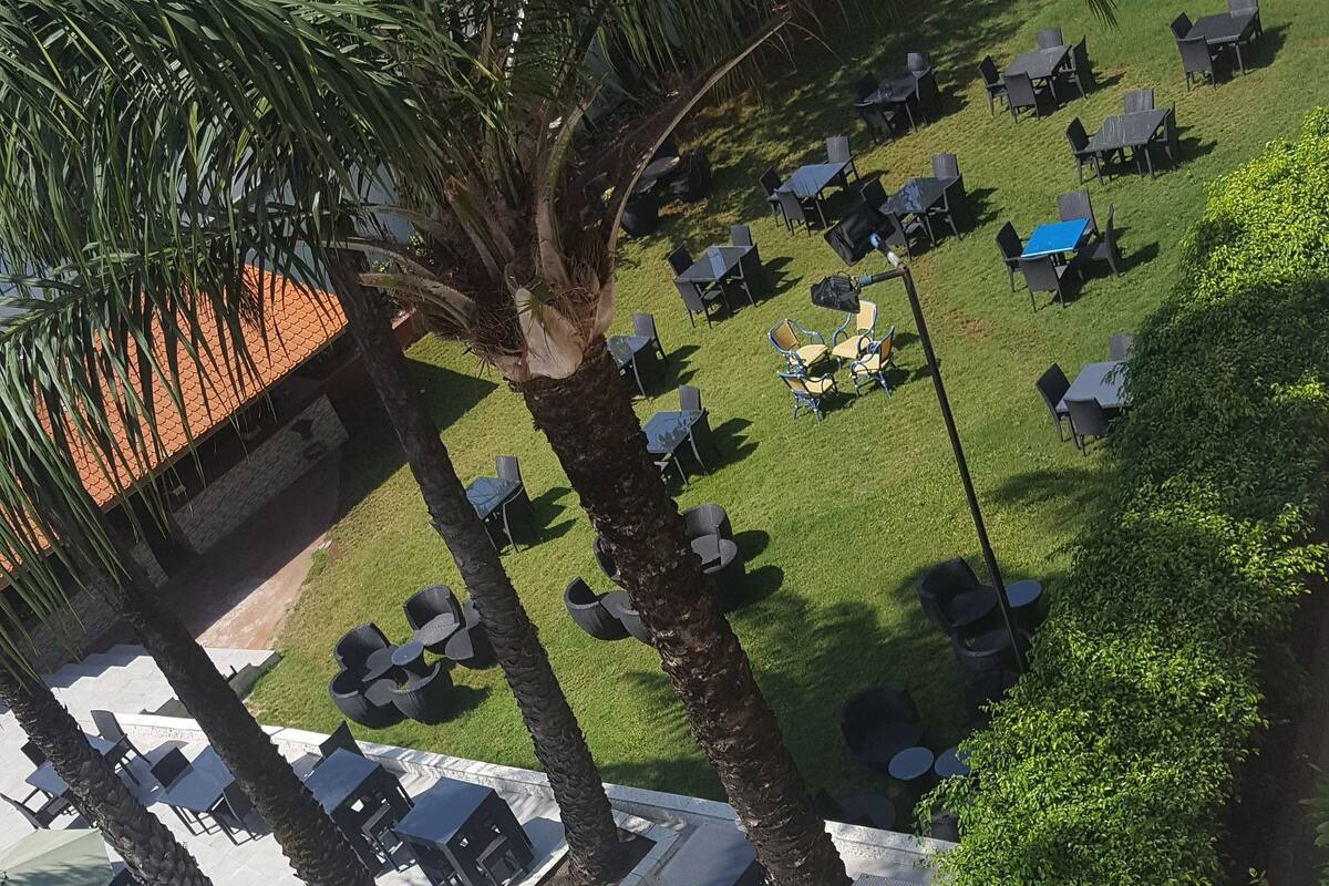 A poolside area with lounge chairs and umbrellas, surrounded by palm trees and a tiled patio.
