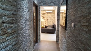 A narrow hallway with textured stone walls leading to a living area with a sofa and curtains. - Riviera Taouyah Hotel (Conakry)