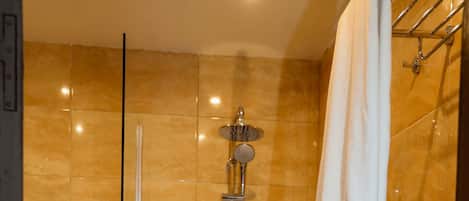 A shower area with a glass door, a handheld showerhead, and a towel rack.