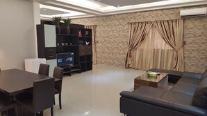 A modern living room with a flat-screen TV, a sofa, a dining table, and a cabinet. - Riviera Taouyah Hotel (Conakry)