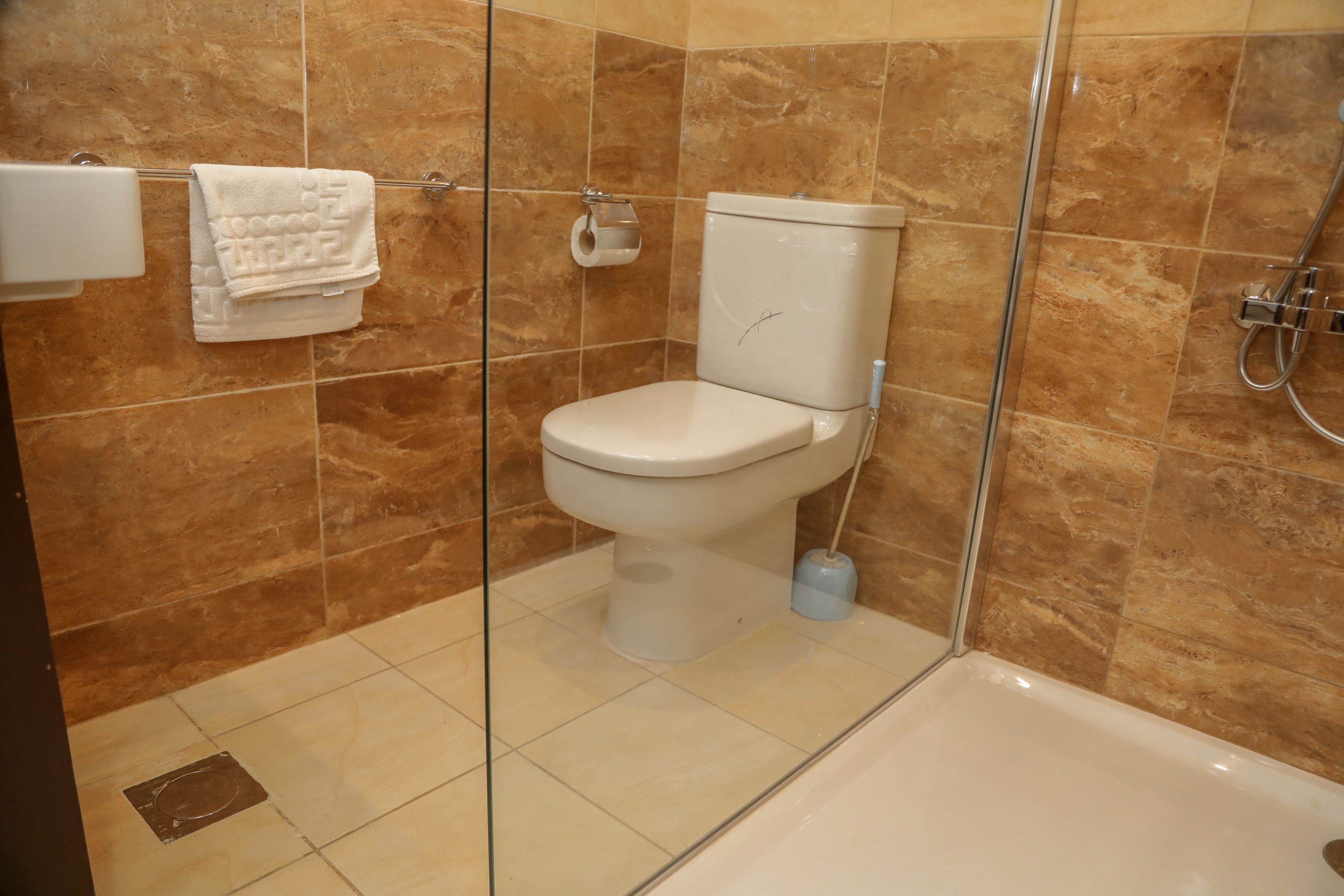 A bathroom with a toilet, a glass shower enclosure, and a tiled floor.