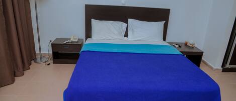 Una habitación de hotel con una cama, una mesita de noche, una lámpara y una cortina.