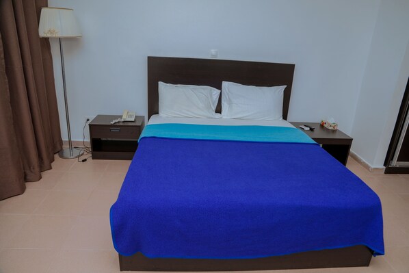 A hotel room with a bed, a nightstand, a lamp, and a curtain.