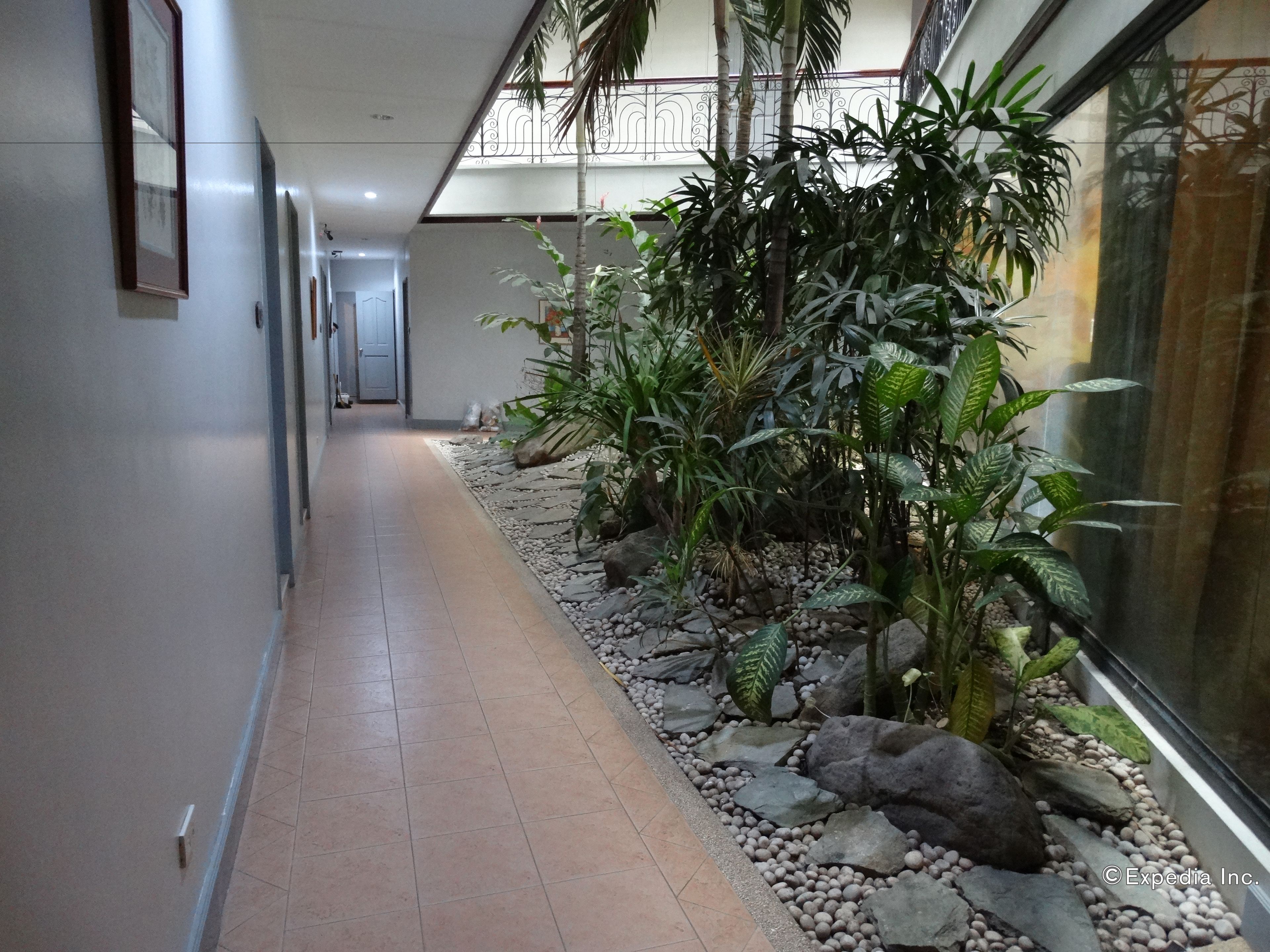 A corridor with a tiled floor, a glass wall on one side, and a row of plants and rocks along the right.
