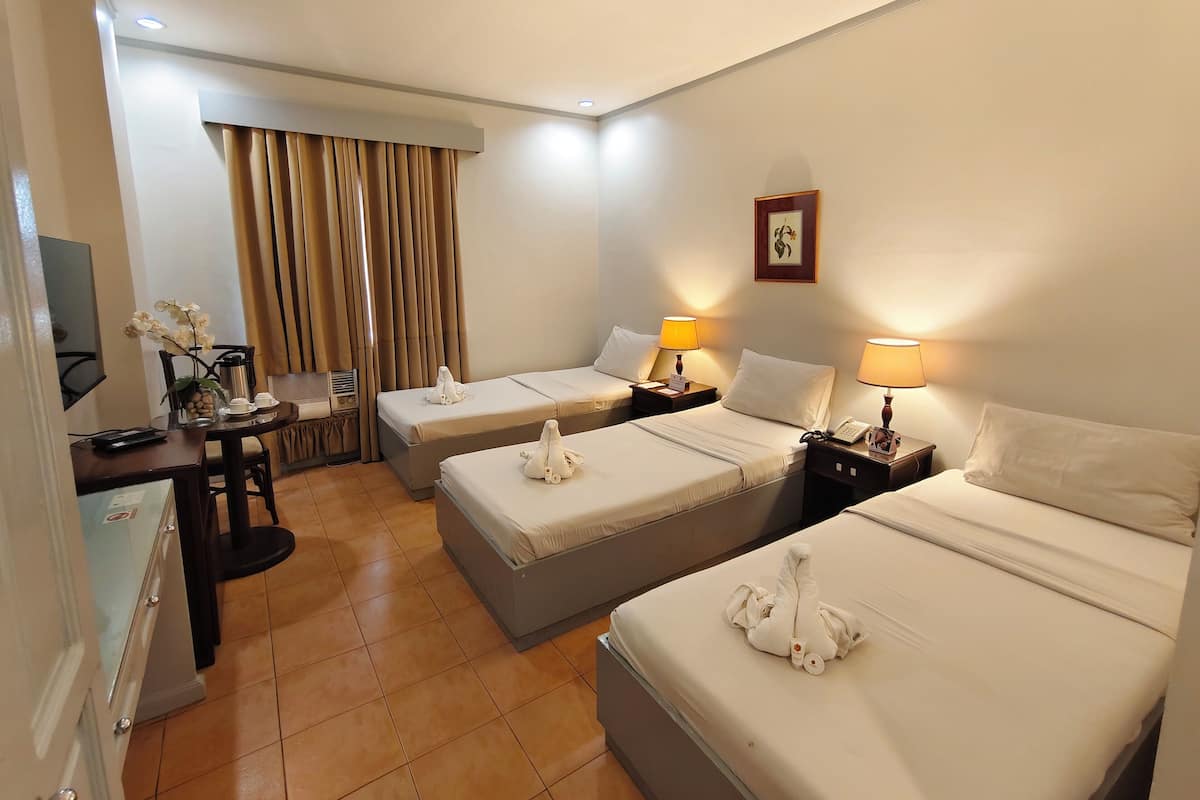 Habitación de hotel con dos camas, un escritorio con silla, televisión y ventana con cortinas.