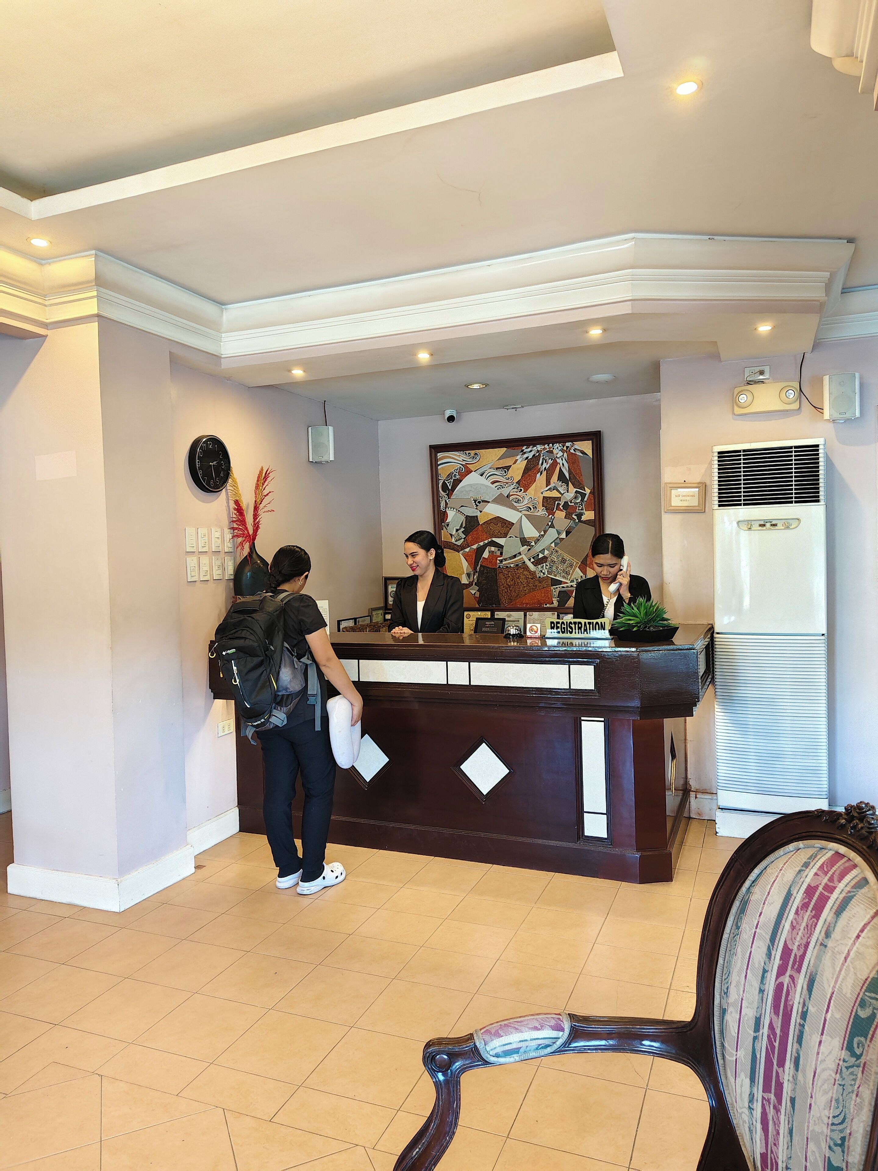 A reception desk with a clock, a framed artwork, and a registration sign.