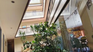 A corridor with a skylight, indoor plants, and a seating area with a view of the restaurant. - Casa Leticia Business Inn (Davao)