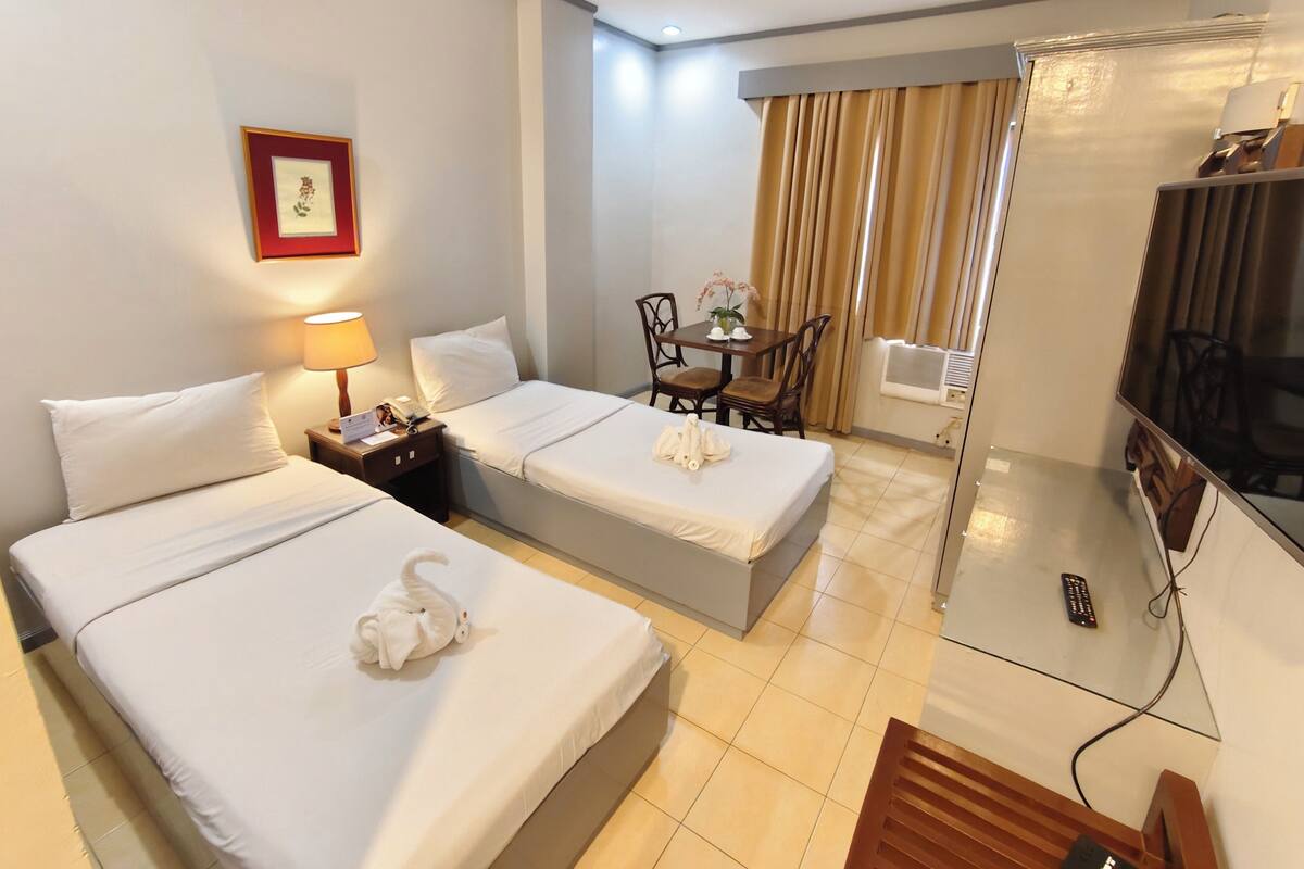 Habitación de hotel con dos camas, un escritorio, una silla, un televisor y una ventana con cortinas.