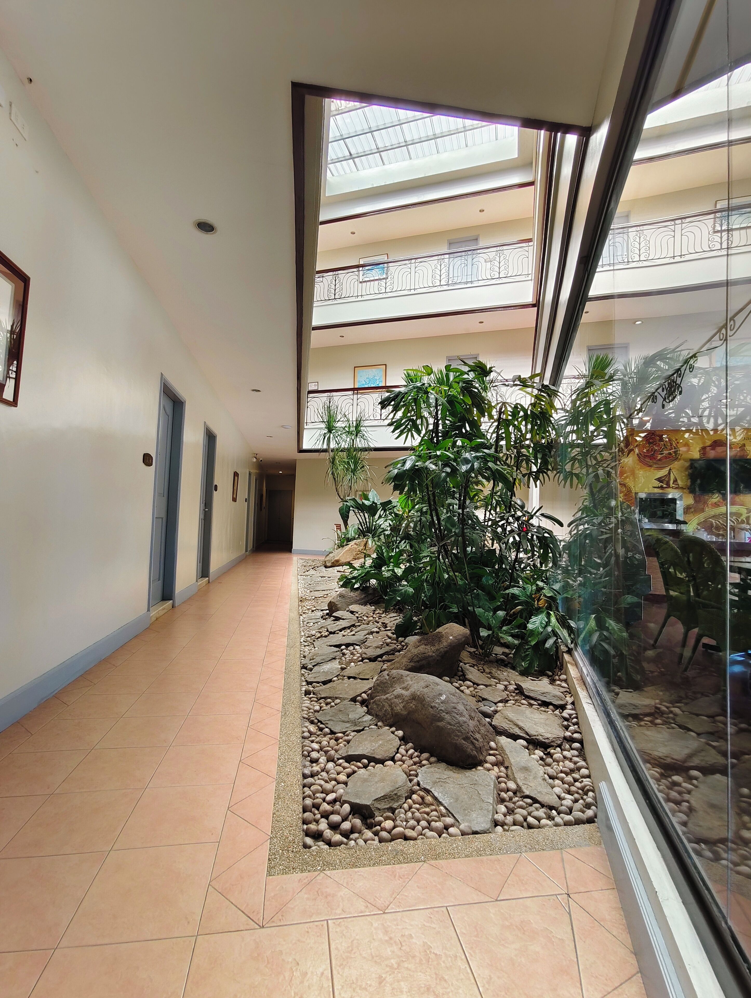 Un couloir doté d’une rambarde en verre, un jardin de roches et de galets, et une vue sur l’étage supérieur.