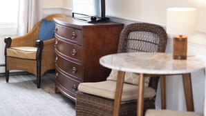 A room with a wooden dresser, a television, wicker chairs, a small round table, and a lamp. - Inn at 7 Central (Provincetown)