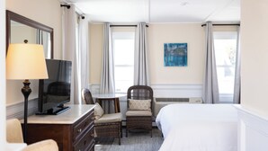 A hotel room with a bed, a television, a chair, a dresser, and a painting on the wall. - Inn at 7 Central (Provincetown)