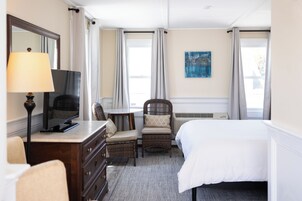Habitación de hotel con cama, televisión, silla, cómoda y un cuadro en la pared.