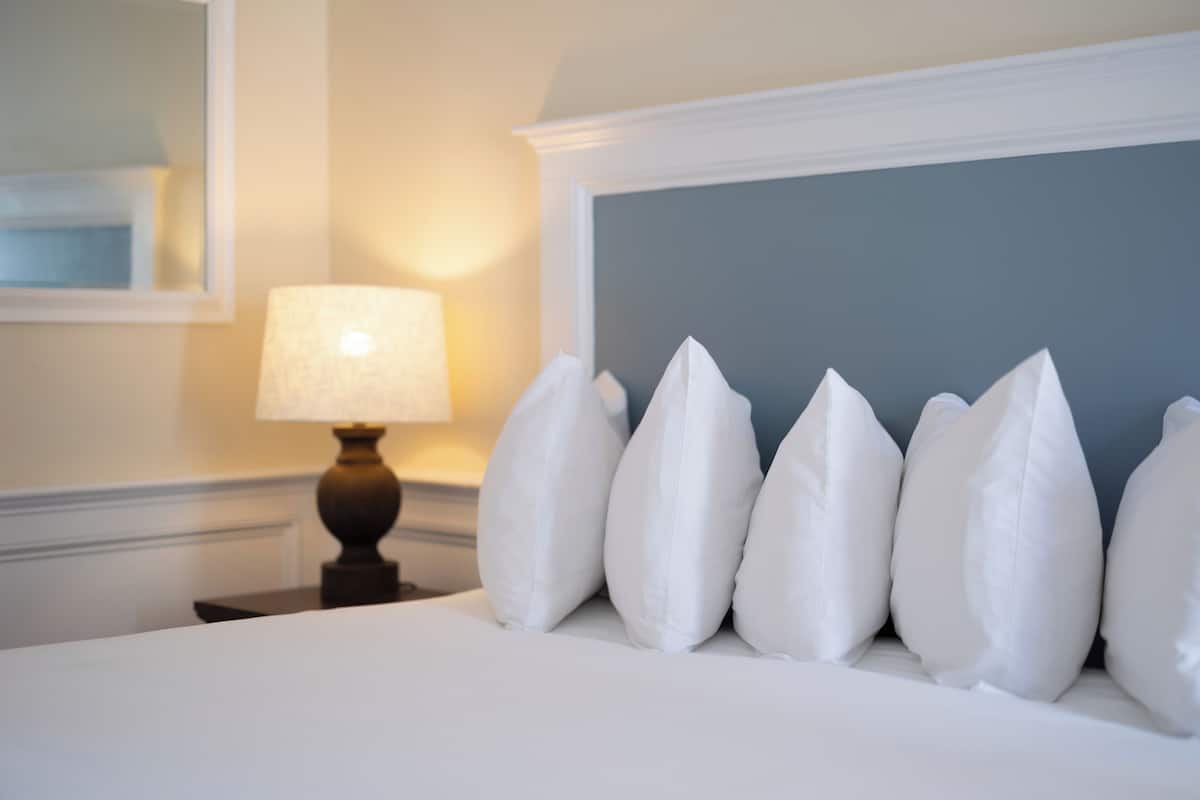 A neatly made bed with white pillows and a lamp on a bedside table.