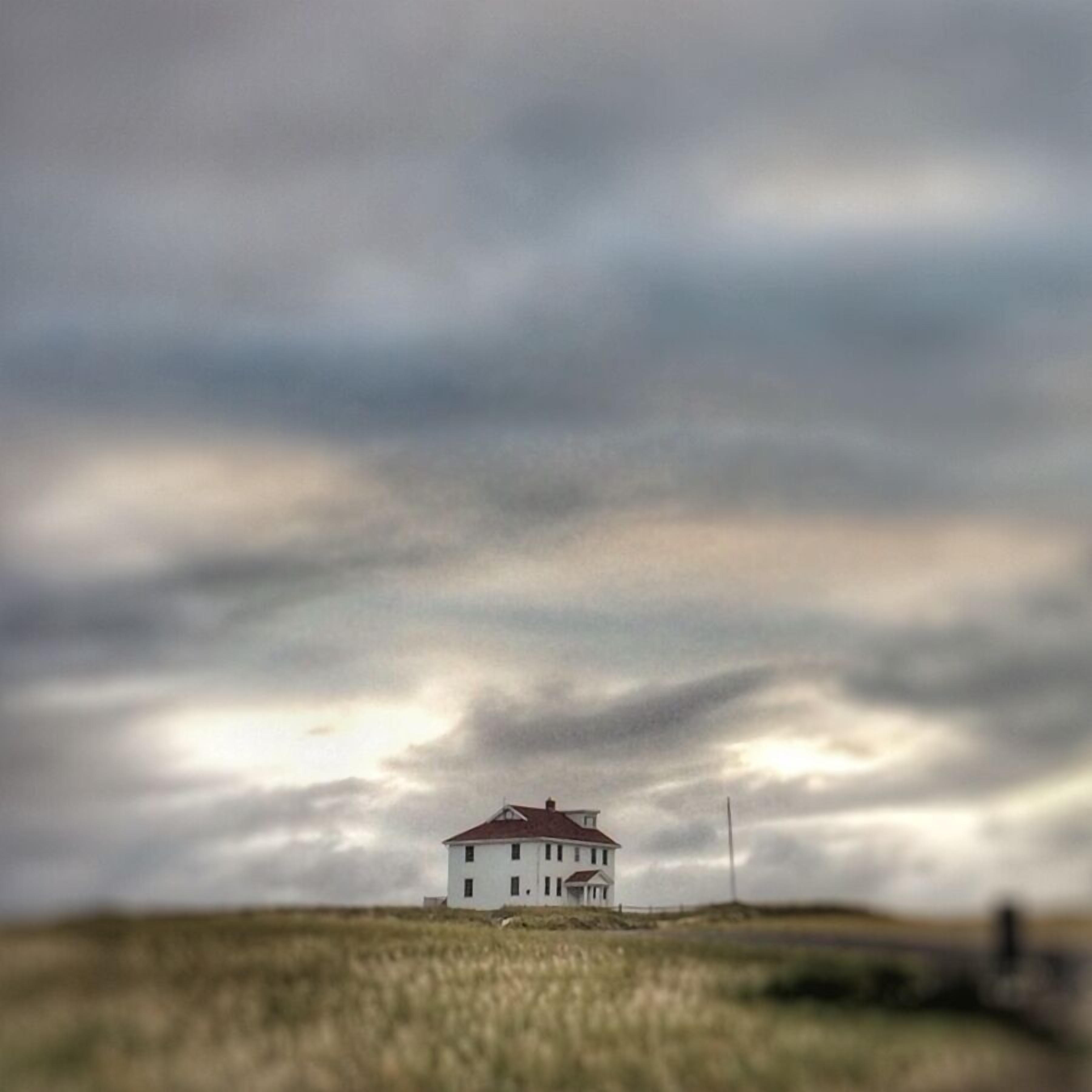 Een wit gebouw met een rood dak, omgeven door grasland onder een bewolkte lucht.