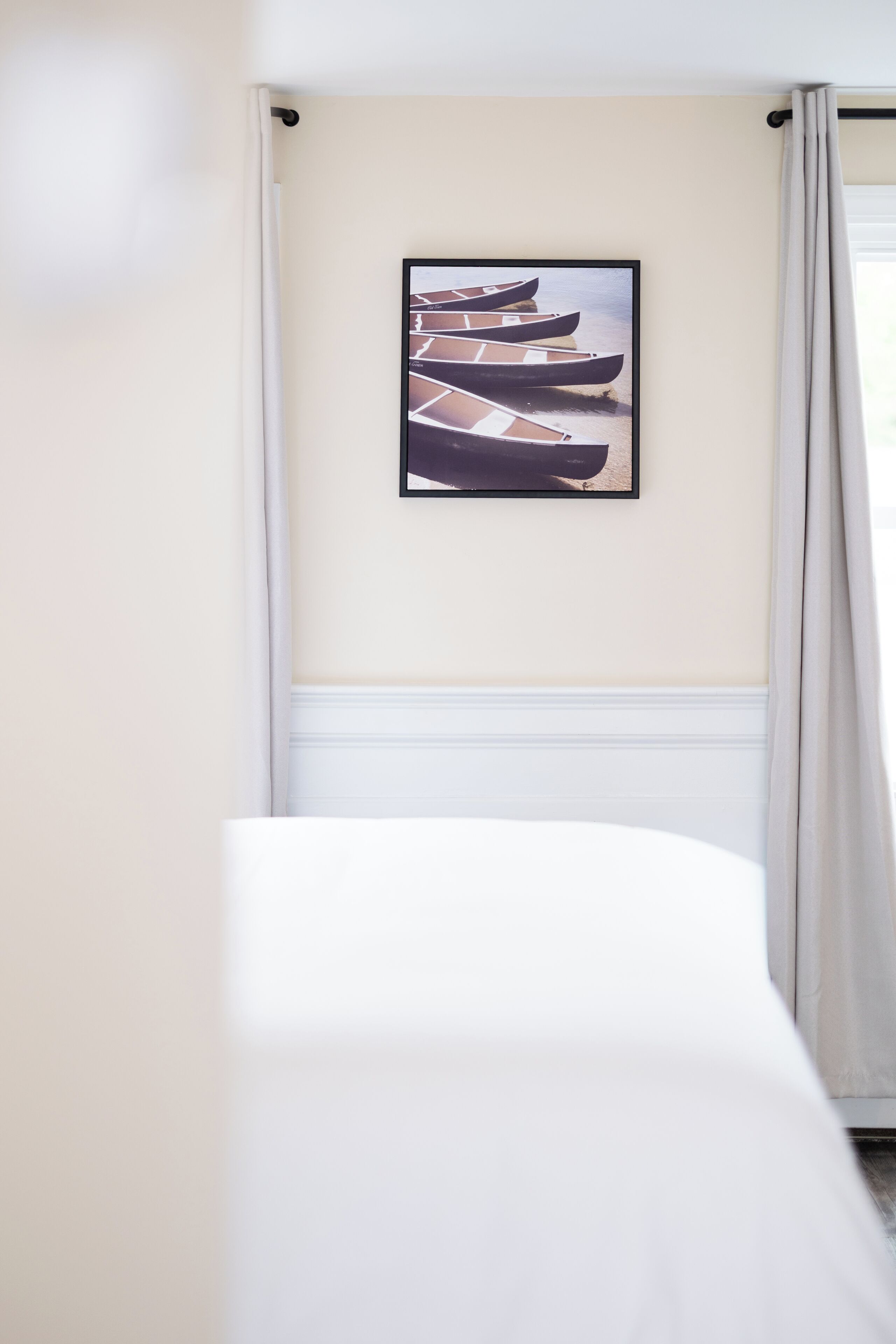 A room with a bed, a framed picture of boats on the wall, and a window with curtains.