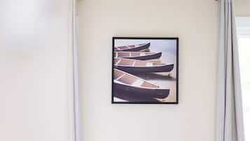A room with a bed, a framed picture of boats on the wall, and a window with curtains.