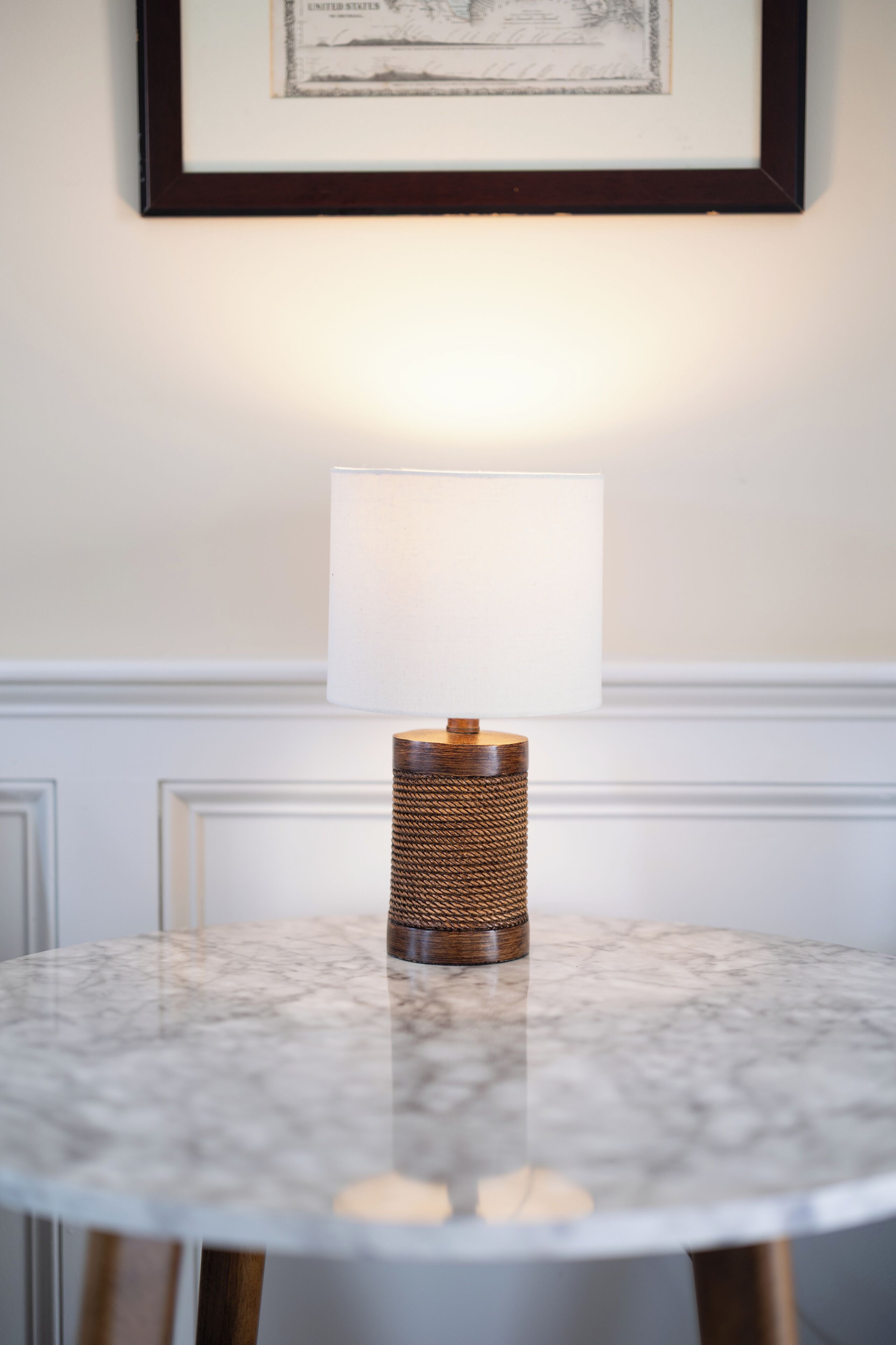 A round marble table with a woven lamp base and a white lampshade.
